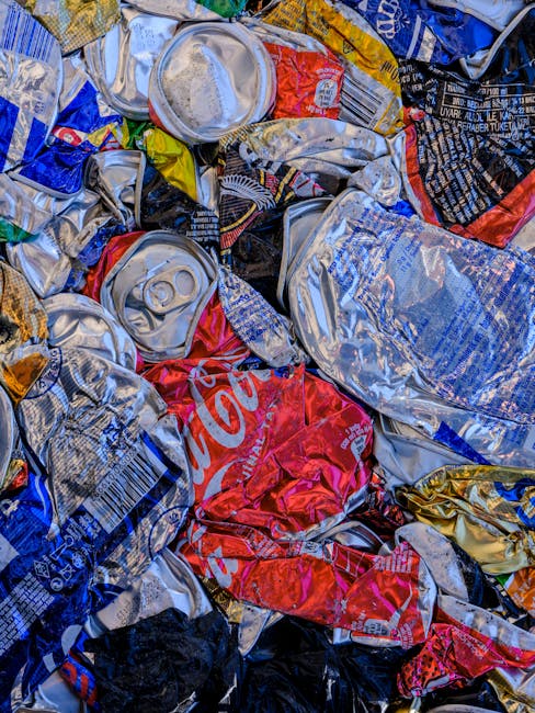 A person’s hand is extending from the left side of the image, holding a green and blue plastic bag filled with household rubbish, such as crumpled paper or other waste materials. The bag is tied at 