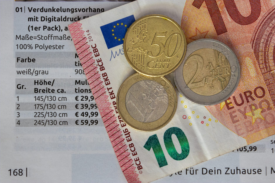Close-up image showing a black calculator with blue and white keys, positioned in the upper left corner of the frame. To the right of the calculator, there are three distinct stacks of euro coins arra